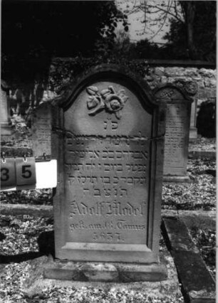 Grabstein 35 (Index: 99796609) Material: Sandstein Zustand: quer gebrochen, repariert Maße HxBxT: 96x46x12 cm Beschreibung: Stele, Sockel, Konvexbogenabschluß, Schrift eingetieft Symbolik: geknickte Rose: Grabstein 35