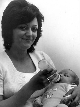Eine stolze Mutter gibt ihrem Baby das Fläschchen. Das Baby scheint zufrieden zu sein