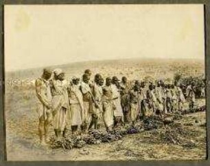 Afrikanische Männer, in einer Reihe vor Bananen und Krügen stehend