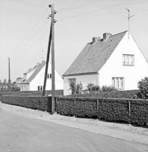 Wiesenweg: Neubausiedlung: Einfamilienhäuser mit Vorgärten, Hecken und Zäunen: vorn Straße: links Strommasten
