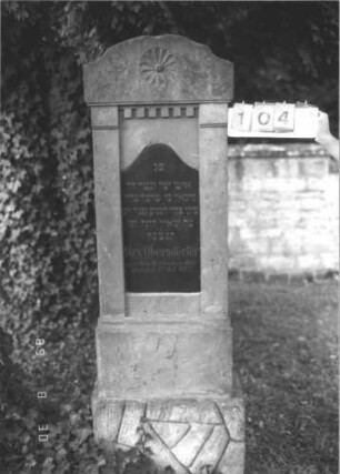 Grabstein 104 (Index: 99609740) Material: Sandstein, Inschriftplatte Granit Zustand: leicht verwittert Maße HxBxT: 192x62x26 cm Beschreibung: Stele, schräg eingezogener flacher Segmentbogenabschluß, eingelassene Schrifttafel mit Konvexbogenabschluß, getreppter Sockel, unten rusticaartig Symbolik: Rosette: Grabstein 104