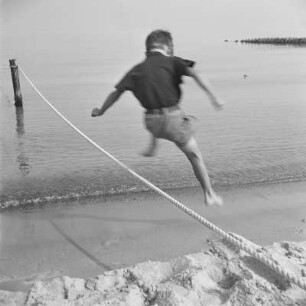 Kind der Gremmlers springt über ein aufgespanntes Seil am Strand von Henkenhagen (heute: Ustronie Morskie)