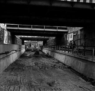 Pölitzer Weg: Bahnunterführung: Ausbau des Tunnels: Bagger beim Ausschachten unter der Unterführung: in der Mitte Kanalisationsschacht: rechts und links Fußgängerweg mit Geländer: rechts Paar mit Kind und Kinderkarre: hinten Wohnhäuser: 16. April 1972