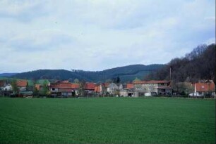 Blick zum Dorf; Häuser, dahinter bewaldete Hügel