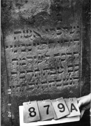 Grabstein 879 (Index: 99751200) Material: Sandstein Zustand: abgeblättert/verwittert Maße HxBxT: 104x58x11 cm Beschreibung: Stele, giebelartiger Abschluß mit Verdachung, Schriftfeld eingetieft: Grabstein 879A