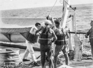 Rettungswesten : Männer beim Anlegen von Rettungswesten vor einem Rettungsboot