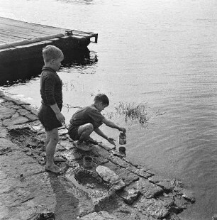 Zwei Jungen spielen am befestigten Ufer eines Flusses