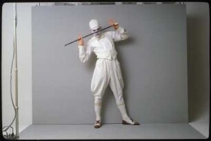 Fotoshooting einer Performance- oder Schauspielgruppe, : Ingolf Thiel in weißem Kostüm, mit Spazierstock und weiß geschminktem Gesicht vor einem grauen Hintergrund