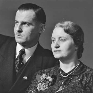 Portrait eines älteren Paares, der Mann trägt einen Zweifinger- oder Hitlerbart und eine Anstecknadel mit Hakenkreuz am Revers