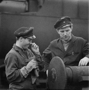 Zwei Eisenbahner zwischen Gleisen im Gespräch, im Vordergrund ein Hülsenpuffer (Serie Deutsche Reichsbahn - Brigade "Otto Buchwitz")