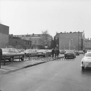 Hagenstraße: Parkplatz mit Pkws: in der Mitte Fußgänger: hinten rechts Firmenschild der Volksbank Bad Oldesloe: links Rückfront der Wohn- und Geschäftshäuser an der Hindenburgstraße: hinten Rückfront des Stadthauses am Marktplatz