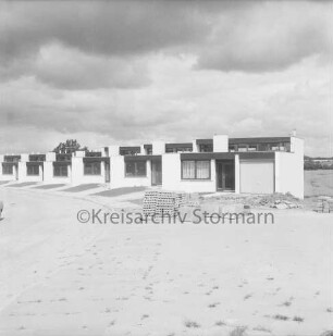 Fuchsberg: Reihenhäuser der Gemeinnützigen Wohnstätten Genossenschaft Bad Oldesloe nach Fertigstellung: vorn unbefestigtes Gelände und Stapel mit Gehwegplatten: 19. Juli 1974