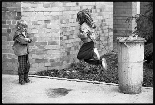 Zwei Mädchen spielen Gummihopse mit einer Mülltonne