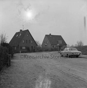 Lorentzenstraße: vor Ausbau: Abrisshäuser mit Garten: rechts Straßenschild und parkender Pkw: links Hecke