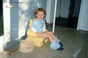 Kleine Schwester mit heruntergelassener Hose auf einem Kinderstuhl sitzend (Altersgruppe bis 14)