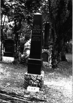 Grabstein 102 (Index: 100101599) Material: Granit, unterer Sockelteil Kalkstein Zustand: gut Maße HxBxT: 230x44x36 cm Beschreibung: Obelisk, getreppter Sockel, unterer Sockelteil rusticaartig Besonderheit: Doppelgrab für Eheleute: Grabstein 102