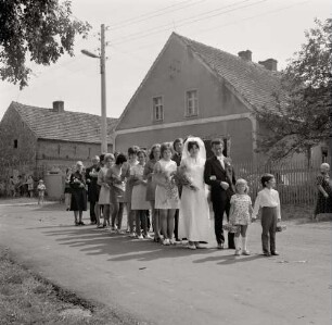 Fotografie eines Hochzeitszuges auf einer dörflichen Straße