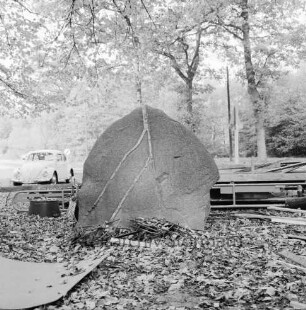 Wöhrendamm / Waldreiterweg: vorn Findling mit Gesteinseinschlüssen: dahinter Förderband: hinten rechts VW-Käfer: hinten rechts zwei Bäume und Verkehrsschild: dahinter Wald