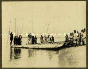Schutztruppenoffizier mit Askaris und afrikanischen Kahnschiffern bei Einbaumbooten am Ufer