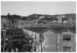 Genua/ Italien: Hafengelände. Blick über Lagerhallen, Lastkran mit Booten und Gütern gegen Häuser auf Hügel der Stadt