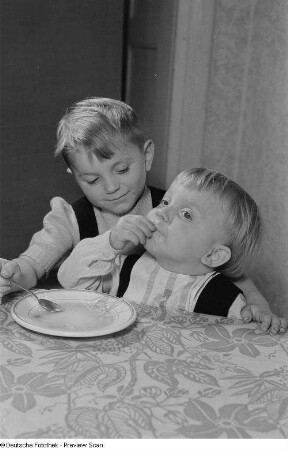 Ein Kind beim Füttern eines Jüngeren mit Nudelsuppe