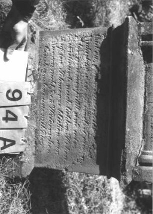 Grabstein 94 (Index: 99787177) Material: Sandstein und aufgesetzter Zapfen aus Metall Zustand: stärker verwittert am Sockel Maße HxBxT: 142x57x18 cm Besonderheit: Schrift schwarz: Grabstein 94A