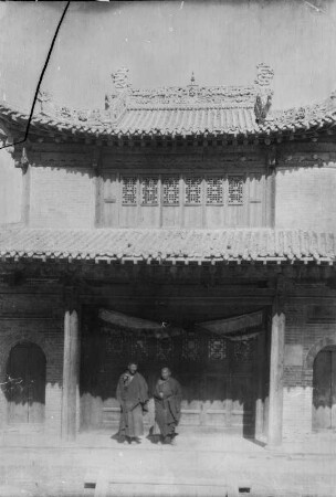 Doppelportrait : Portrait zweier Männer aus Zentralasien vor einem Gebäude im chinesischen Baustil, vermutlich vor einer Tempelanlage im Tian Shan Hochgebirge