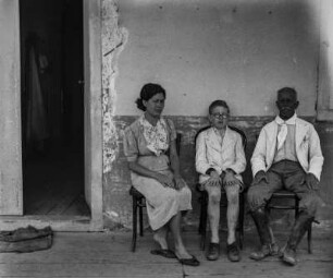 Portraitaufnahme : Portrait einer Frau, eines Jungen und eines Mannes auf Stühlen sitzend vor einer Wand.