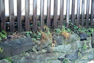 Natursteinmauer unter einem Zaun