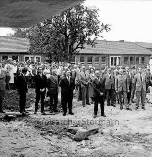 Volksschule am Schweinemarkt [später Emil-Nolde-Schule]: Erweiterungsbau: Richtfest: auf Hof: Gemeindevertreter, Elternbeirat, Lehrer, Verwaltung und Schüler lauschen dem Richtspruch, darunter Bürgermeister Karl Eduard Claussen, Hans-Heinrich Gaycken: im Hintergrund Baum, Schulpavillon: im Vordergrund oben links überhängendes Dach