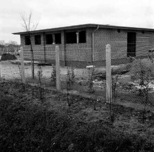 Sporteinrichtungen: Sportplatz: Neubau: Umkleidehaus im Rohbau: im Vordergrund Zaun, dahinter Gartenanlage