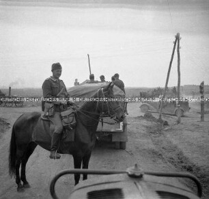 Rumänischer Soldat auf einem Pferd und LKW der Wehrmacht auf einer Landstraße, aus einem LKW heraus fotografiert