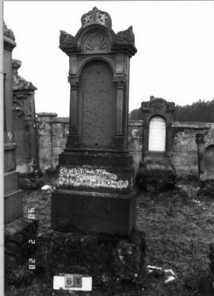 Grabstein 61 (Index: 100114623) Material: Sandstein Zustand: Stele verrutscht, Textplatte fehlt Maße HxBxT: 258x70x29 cm Beschreibung: Ädikula mit Sockel auf Rustikasockel, überstehender, eingezogener Rundbogen mit Konche und Akroteren, eingesetzte Textplatte Symbolik: Konche: Grabstein 61
