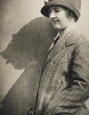 Portrait einer jungen Frau. Sie trägt ein Kostüm und einen Hut
