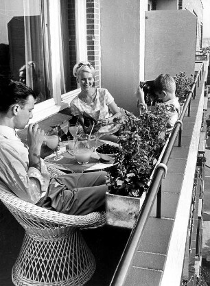Eine junge Familie befindet sich auf dem Balkon. Es wird Saft getrunken. Obst steht auf dem Tisch. Ausdruck für eine gesunde Lebensweise