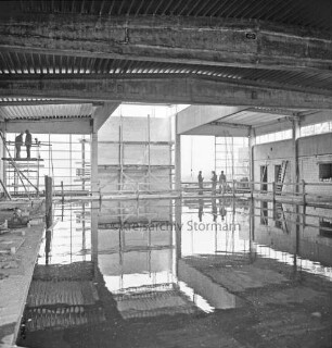 Hallenbad: Soltausredder: Rohbau: Innenansicht: vorn Schwimmbecken mit Wasser: hinten Arbeiter auf Leiter und Gerüst beim Innenausbau: dazwischen Baumaterial