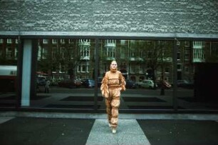 Aufnahme für die Reportagereihe „Außenseiter der Mode“: Studio Fong Leng, Amsterdam : Model in einem gelb-beigen Hosenanzug mit Plissee-Einlagen und Rüschen, nach einem Entwurf von Fong Leng