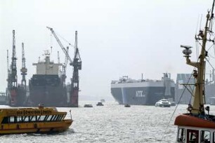 Der Hamburger Hafen ist toll. Ein Car Carrier (Uebersee-Autotransport-Schiff) der NYK Line verlaesst Hamburg auf der Elbe. Links ist das Trockendock 11 von Blohm + Voss zu sehen, darin ein Frachter. Vorn links eine Hafen-Barkasse mit Werbung fuer das Musical Koenig der Loewen. Vor dem riesigen Autotransporter faehrt die Katamaran-Faehre Stade-Hamburg in den Hafen ein