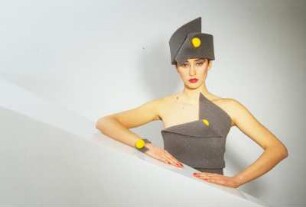 Model in Schaumstoffmode : Model mit schwarzem Schaumstoffhut und -kostüm hinter einem Neonleuchtkörper