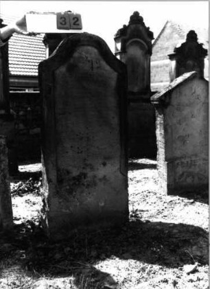 Grabstein 32 (Index: 99797933) Material: Sandstein, weiß Zustand: stark verwittert Maße HxBxT: 129x62x11 cm Beschreibung: Stele, geschweifter Abschluß: Grabstein 32