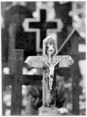 Grabkreuz mit Jesusfigur, im Hintergrund weitere Gräber