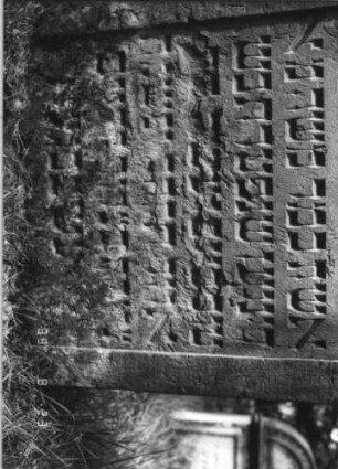 Grabstein 21 (Index: 100110918) Material: Sandstein Zustand: Giebel beschädigt, stärker verwittert mit geringem Textverlust Maße HxBxT: 120x71x11 cm Beschreibung: Stele, Rundbogenabschluß, Schriftfelder eingetieft Symbolik: 2 Rosetten: Grabstein 21A