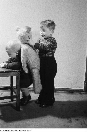 Zwei Kinder, eines spielt mit einem Teddybären
