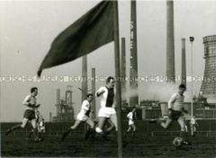 Fußballspielende Männer, im Hintergrund Industriegebiet (Altersgruppe 18-21)