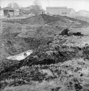 Industriestraße: Absackung eines Teilstücks: vorn Grube mit Wasserloch: dahinter Erdhaufen, Straße: links Arbeiter mit Schubkarre: hinten Wohnhäuser und Gewerbebauten an Pölitzer Weg