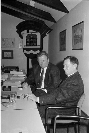 Amtsverwaltung: Wahlen: Amtsvorsteher Frithjof Schumann, erster stellvertretender Amtsvorsteher Harry Gehrken an Tisch: hinten Aufsteller mit Wappen von Gemeinde Trittau