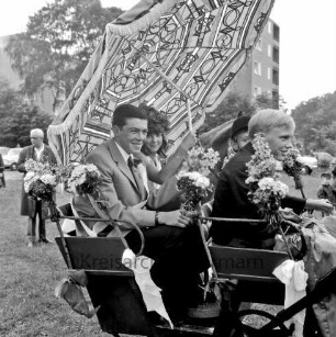 Kindervogelschießen: Festwiese: Festumzug: Hauptkönigspaar Ursula Walch und Norbert Buck unter eienm Sonnenschirm in Kutsche mit Blumenschmuck: im Hintergrund Bäume und mehrgeschossiger Block