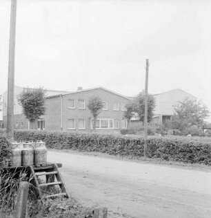 Dorfstraße: Bauerngehöft Leinius: Neubau: davor Hecke und Bäume: links Milchbock mit Milchkannen