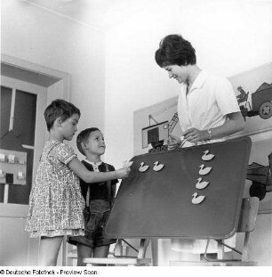 Zwei Kinder mit Erzieherin an einer Magnettafel, erste Mengenaufgaben lösend