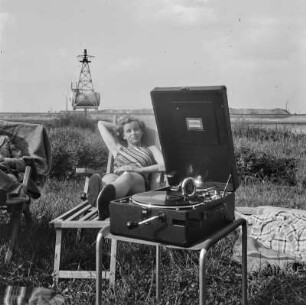 Paar in Liegestühlen im Garten mit Koffergrammophon, im Hintergrund die Leuchtbake Ruge-Egge an der Weser